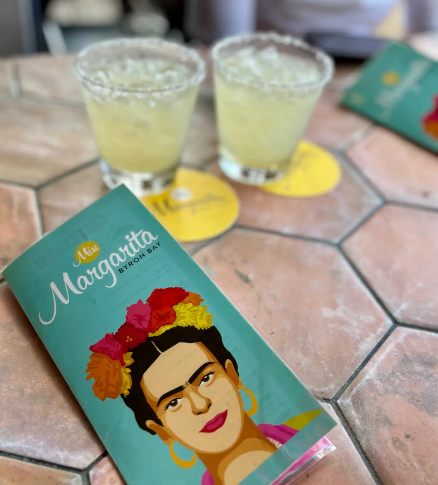 Two margaritas with a Miss Margarita Mexican Cantina menu and coaster on a tiled table in Byron Bay
