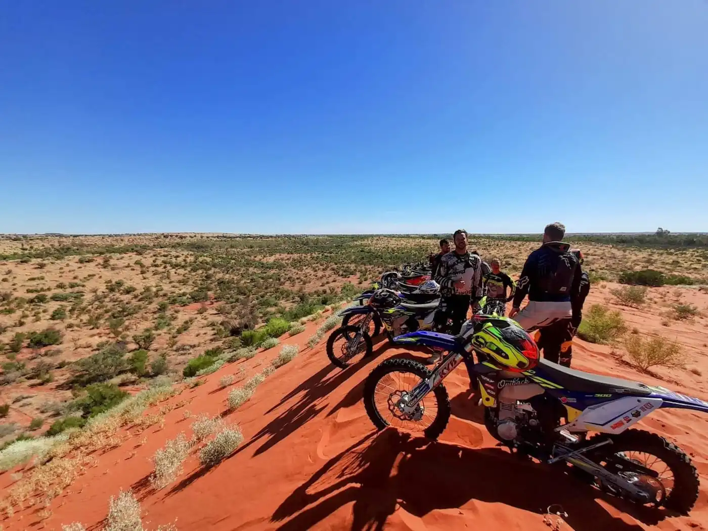 Dirt bike riders overlooking the desert from a red sand dune on the Finke Track